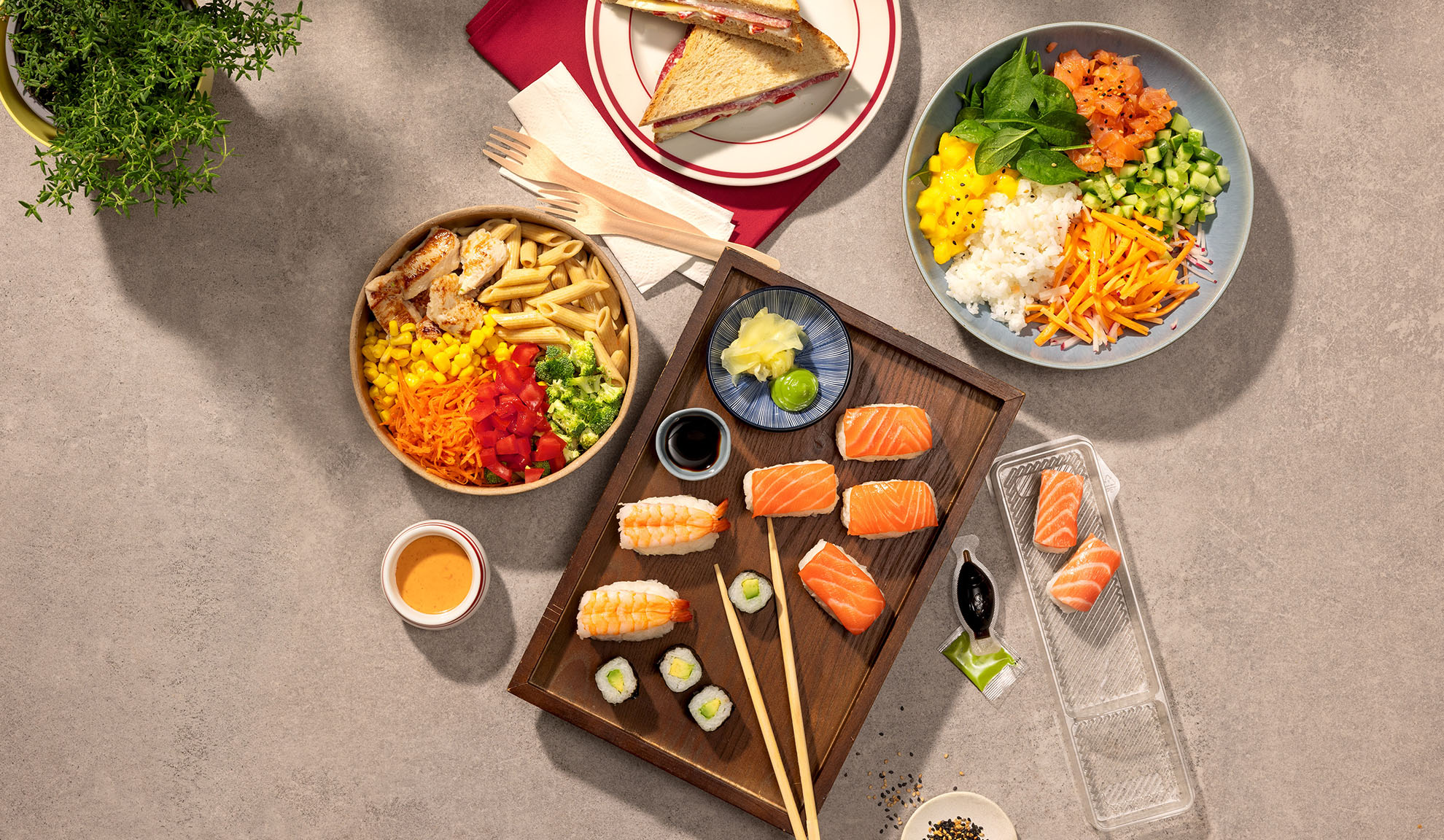 Widok z góry na różne dania na wynos: sushi, poke bowl, sałatka makaronowa i kanapki.