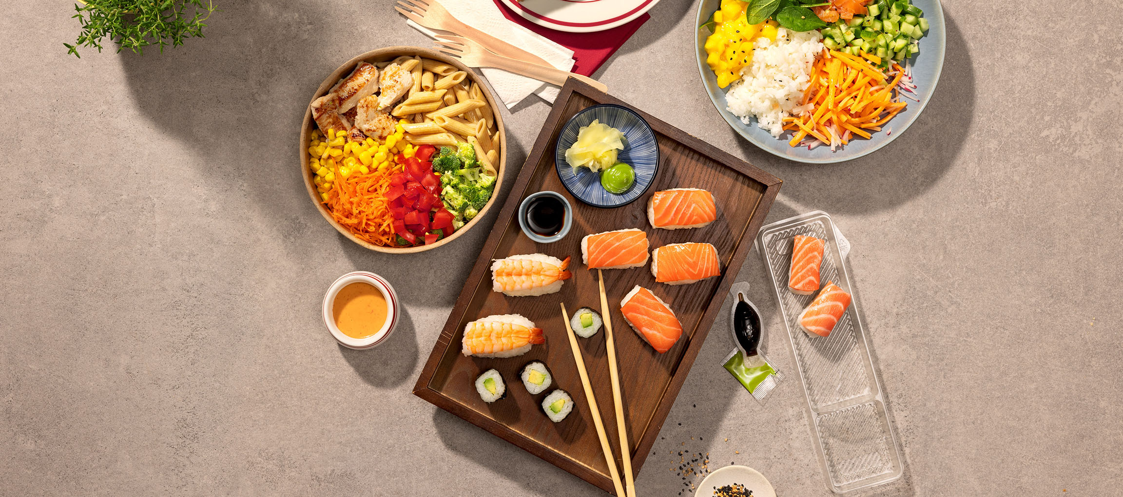 Różnorodne dania: miska makaronu z kurczakiem, sushi i poke bowl na stole.