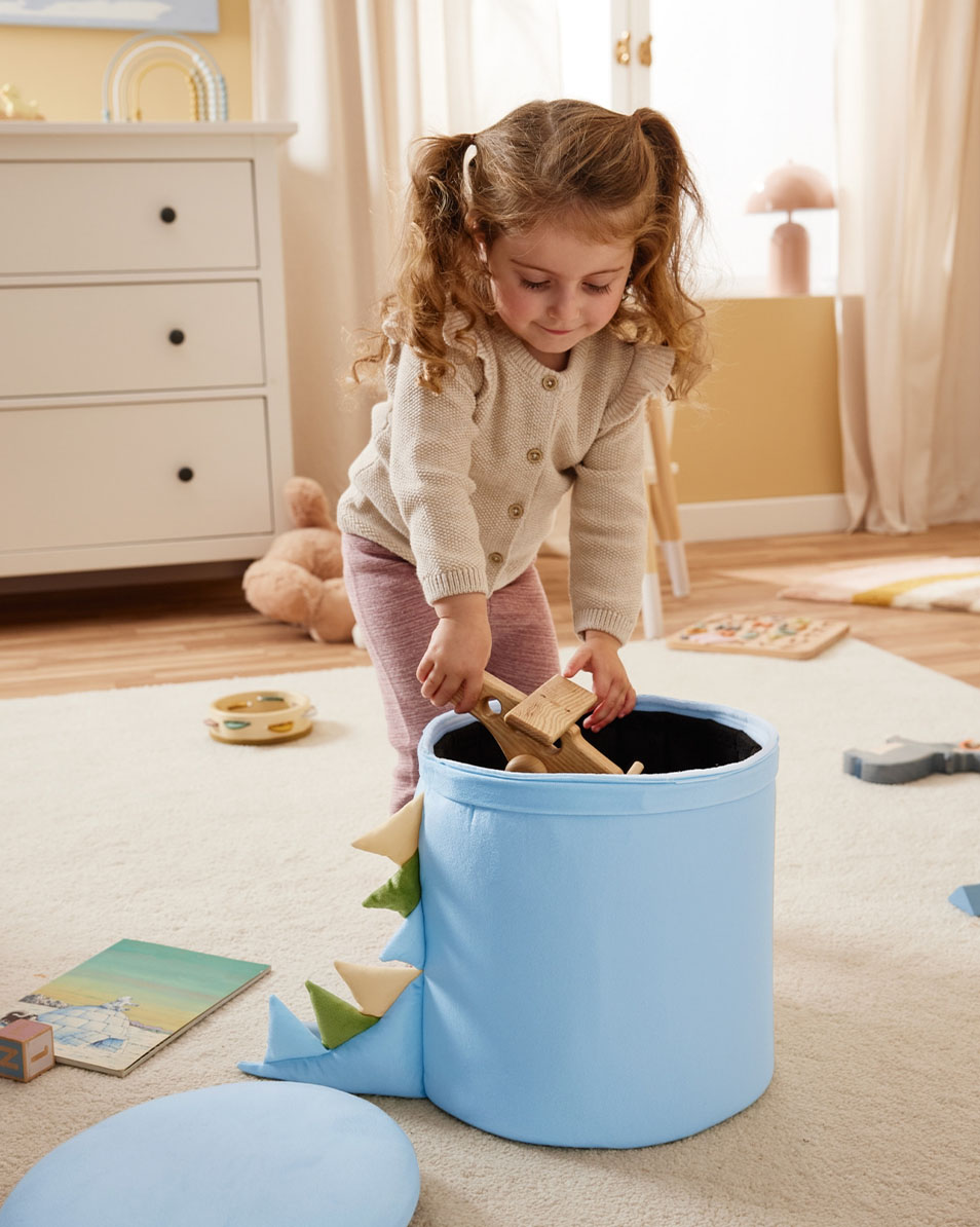 Dziecko wkłada drewniane zabawki do niebieskiego pojemnika do przechowywania w kształcie dinozaura.