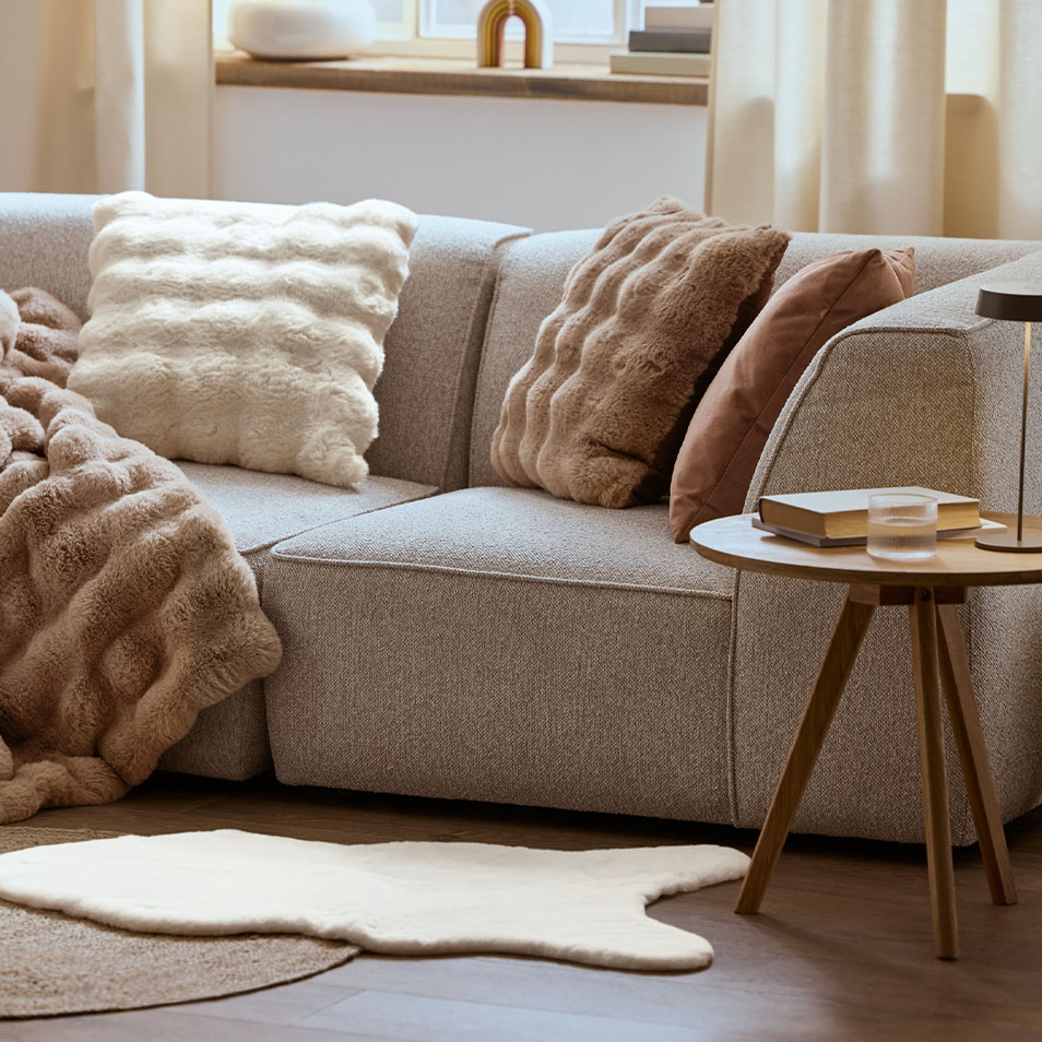 Szara modułowa sofa z puszystymi poduszkami i kocami, obok stolika kawowego.