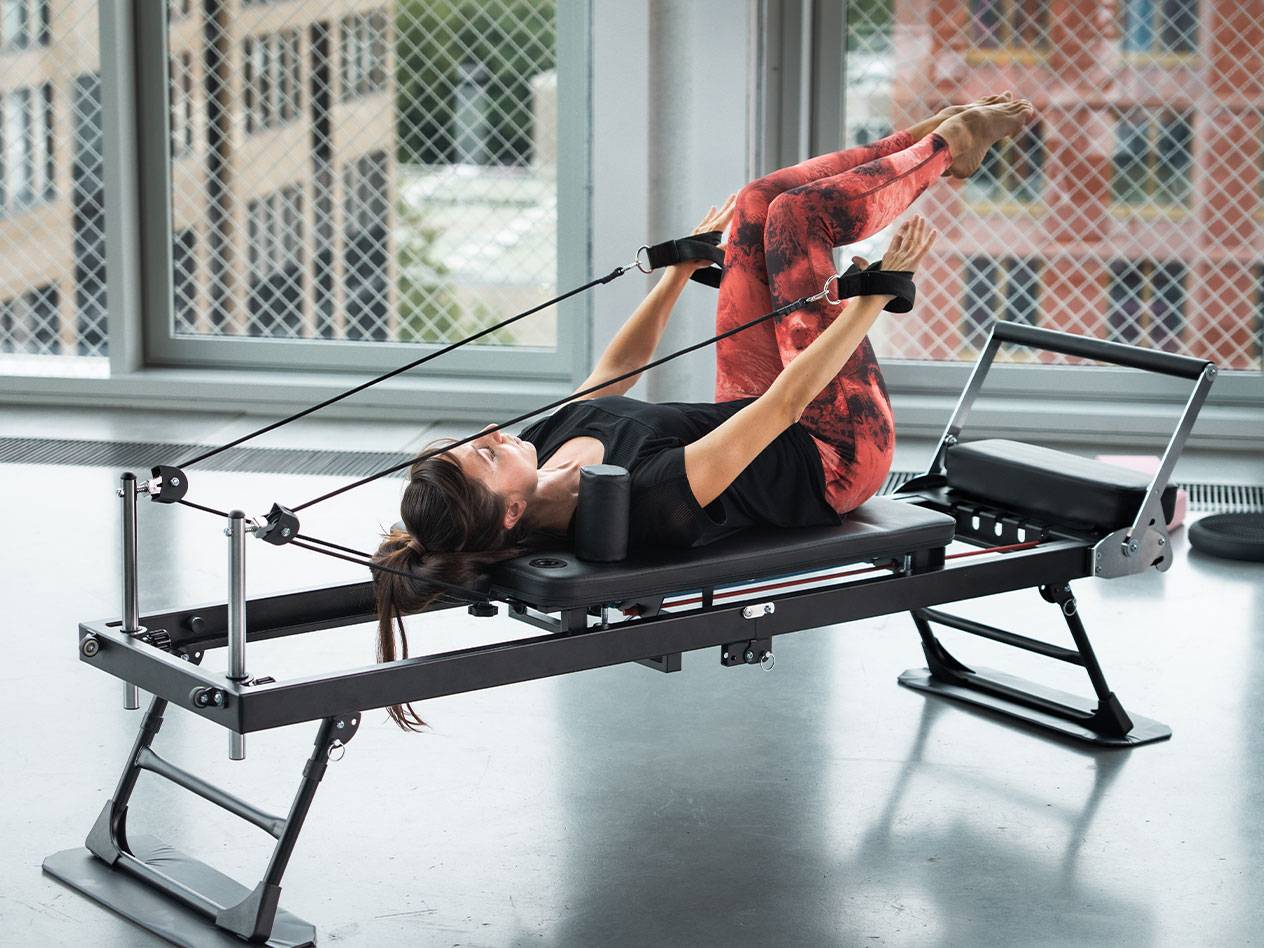 Kobieta ćwicząca Pilates na reformerze w czerwonych legginsach do jogi.