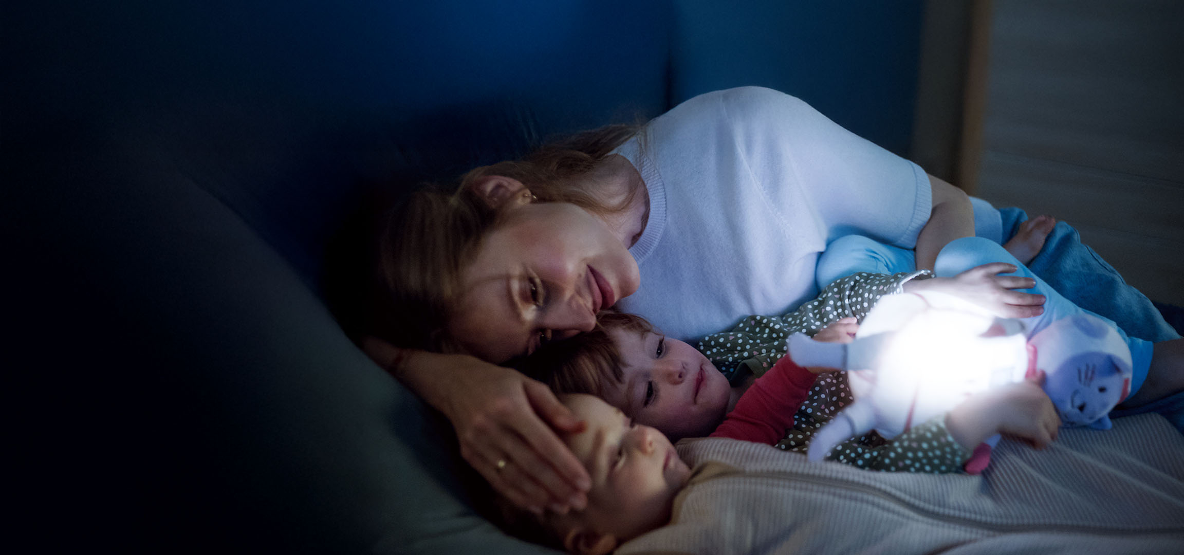 Mama i dwoje dzieci w łóżku ze świecącą zabawką