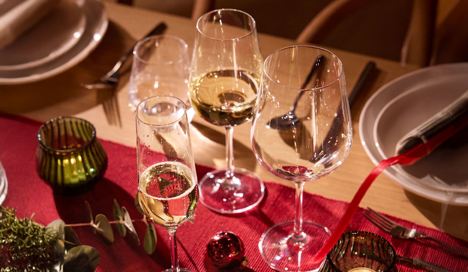 Uroczyście nakryty stół z kieliszkami do wina, kieliszkiem do szampana i dekoracjami świątecznymi.