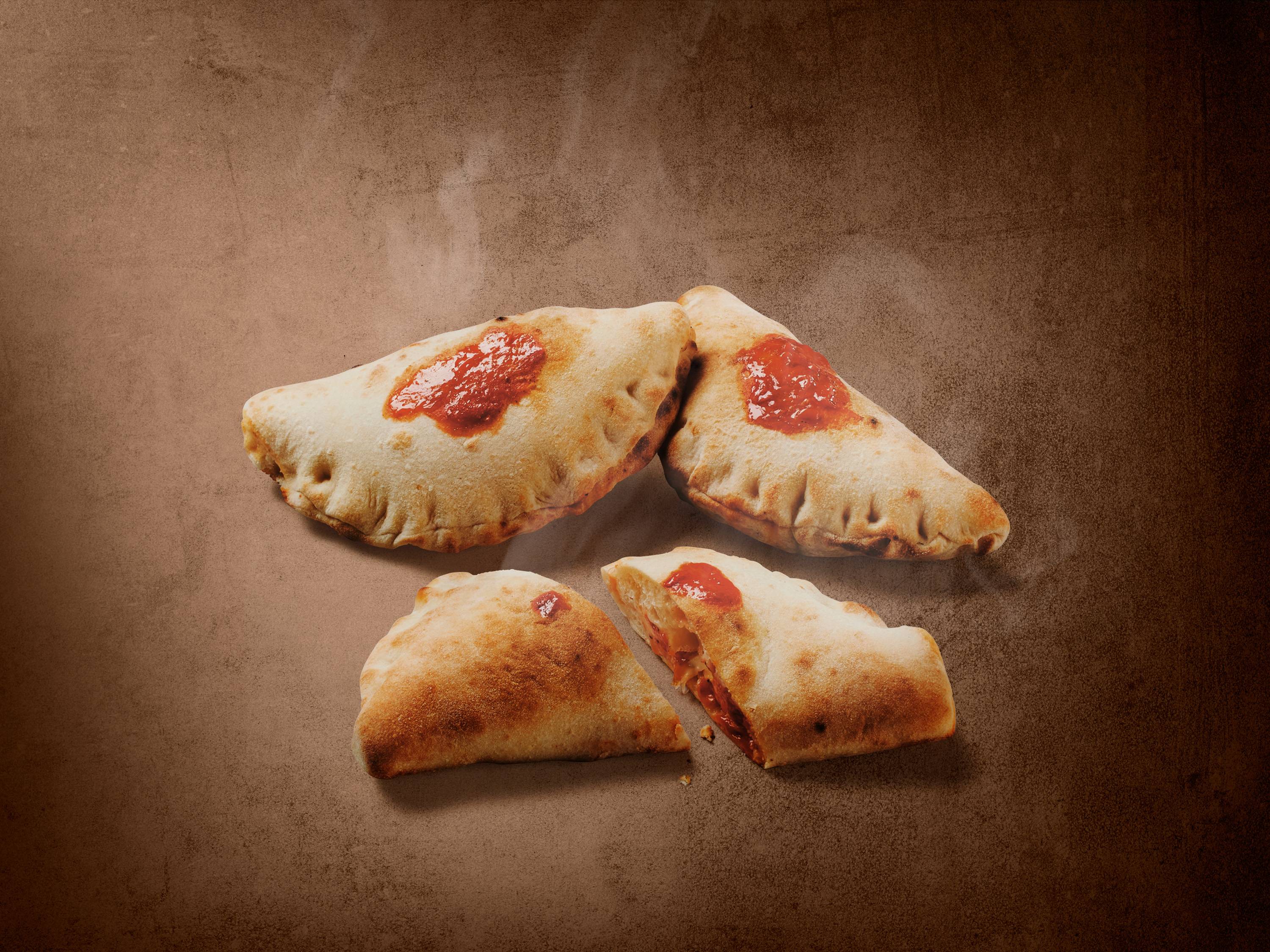 Cztery calzone z sosem pomidorowym na brązowym tle