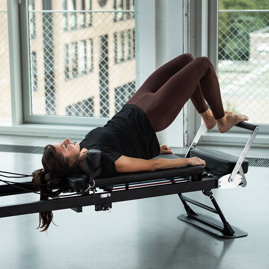 Kobieta ćwiczy Pilates na maszynie reformer, nogi w górze.