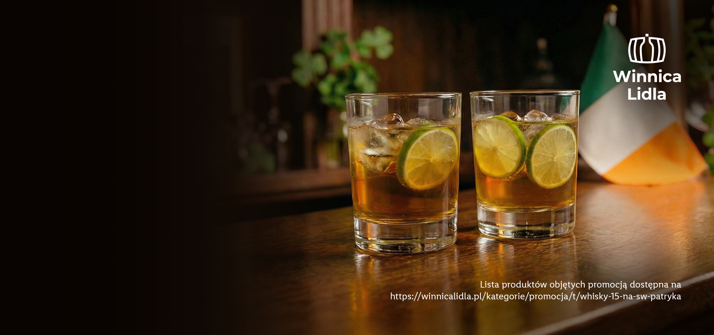 Dwa drinki z whisky i limonką na drewnianym stole, z logo Winnica Lidla i tekstem promocyjnym.