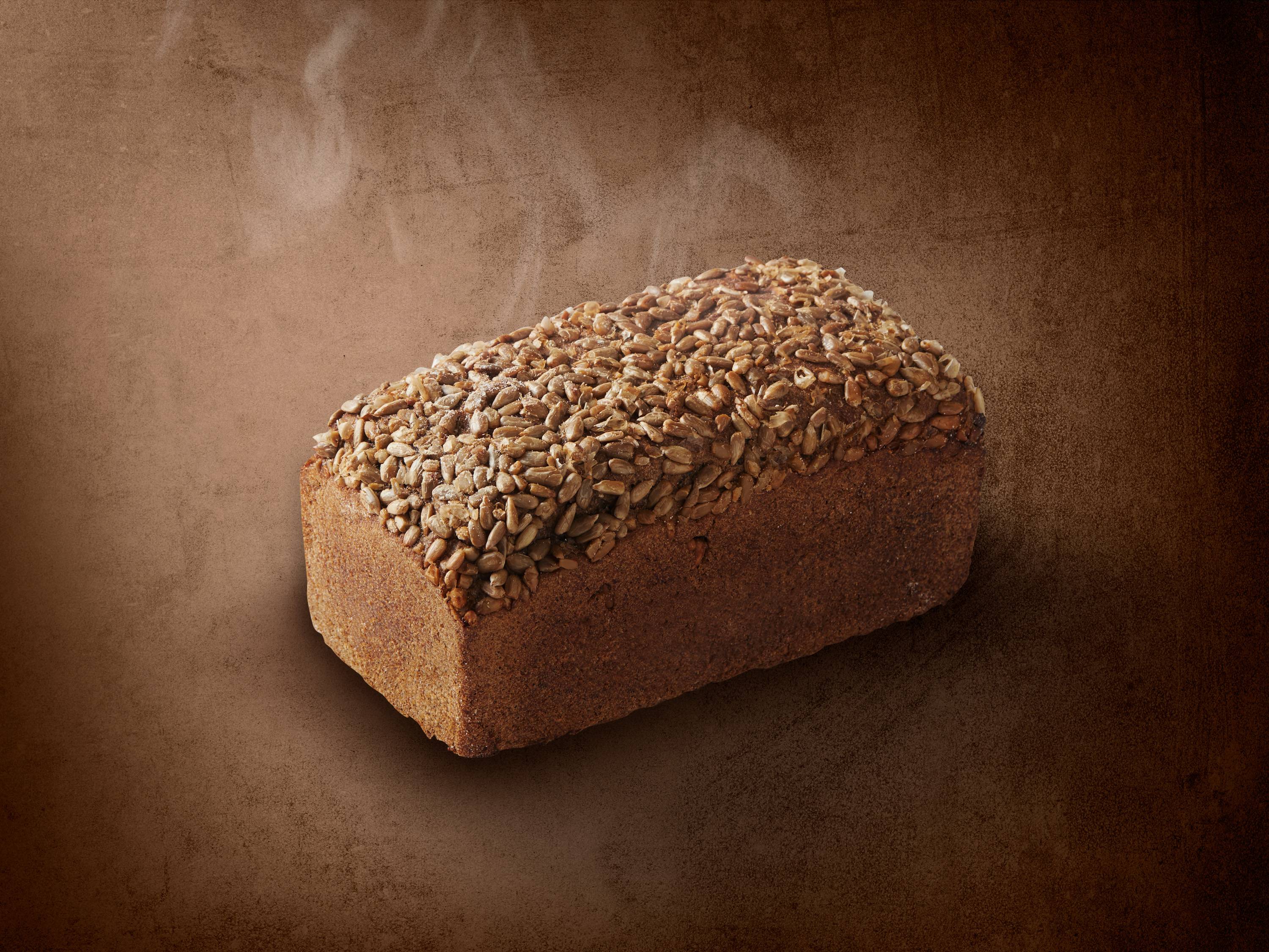 Bochenek chleba z ziarnami słonecznika na brązowym tle z parą