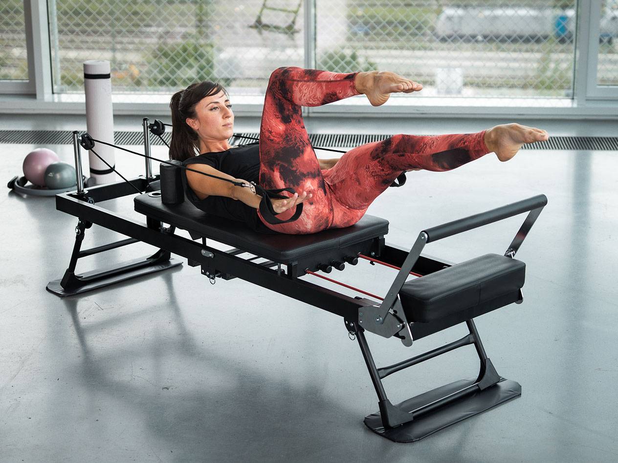 Kobieta ćwiczy Pilates na czarnej maszynie do Pilatesu z czerwonymi detalami.