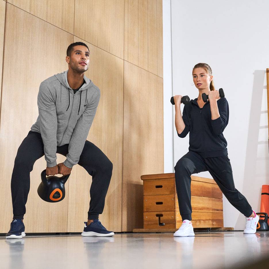 Mężczyzna i kobieta w odzieży sportowej, ćwiczący z kettlebell i hantlami.