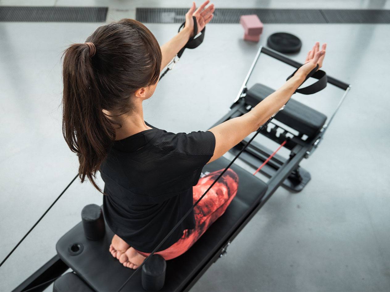 Kobieta ćwiczy Pilates na maszynie reformer z taśmami oporowymi.
