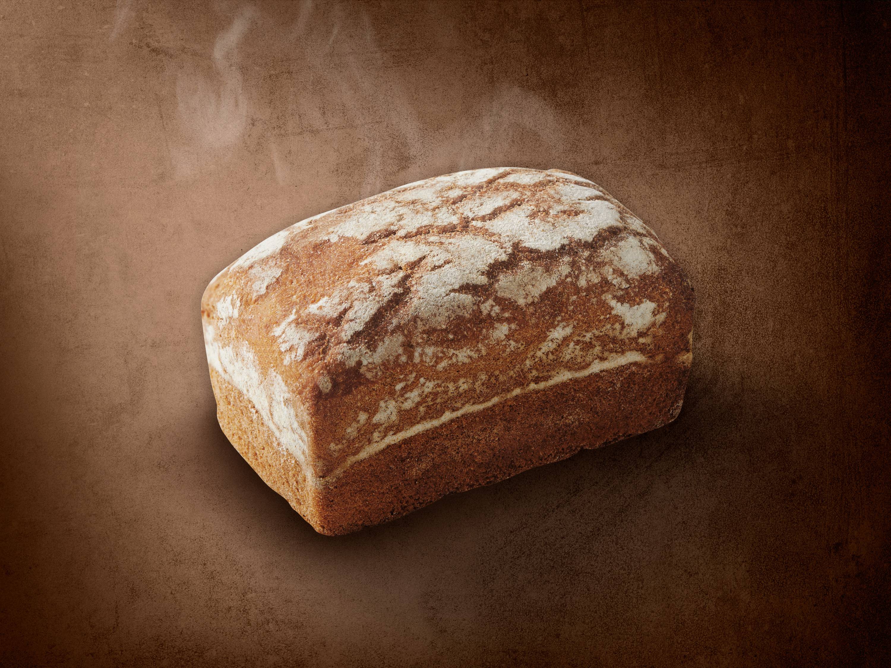 Bochenek chleba z mąką na brązowym tle z parą