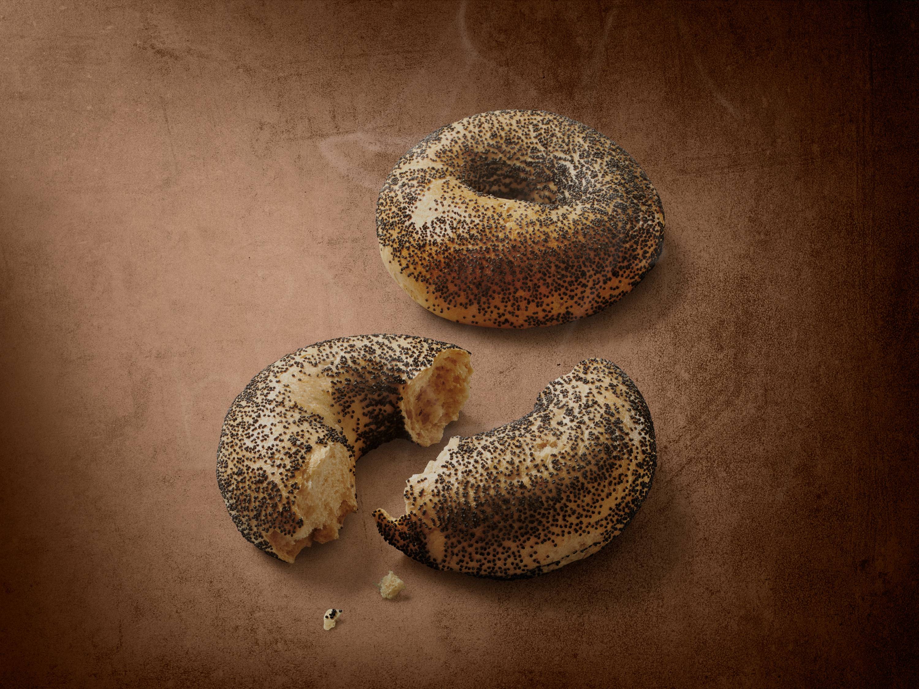 Cały i przełamany bajgiel z makiem na brązowym tle.