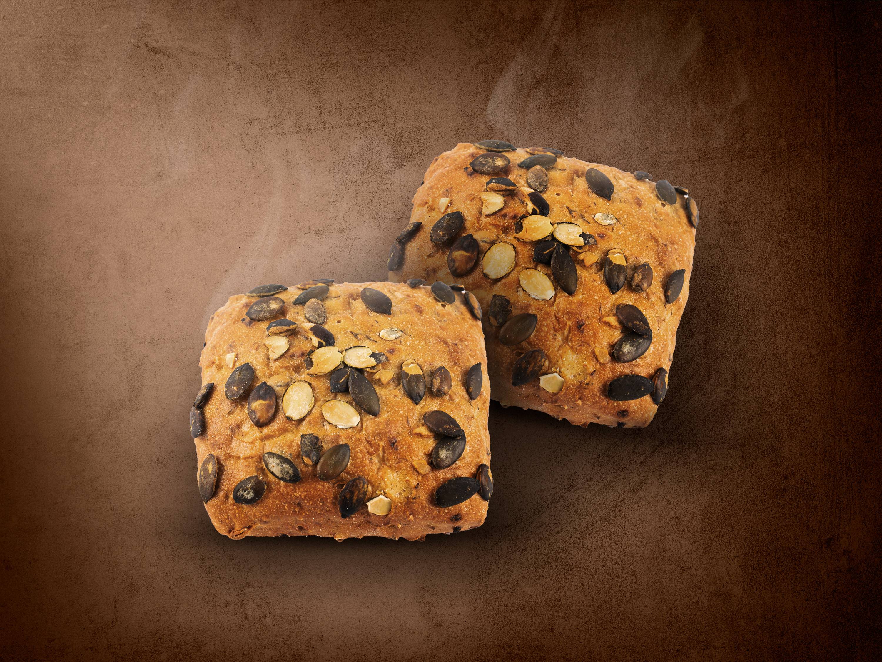 Dwie bułki z pestkami dyni na brązowym tle.