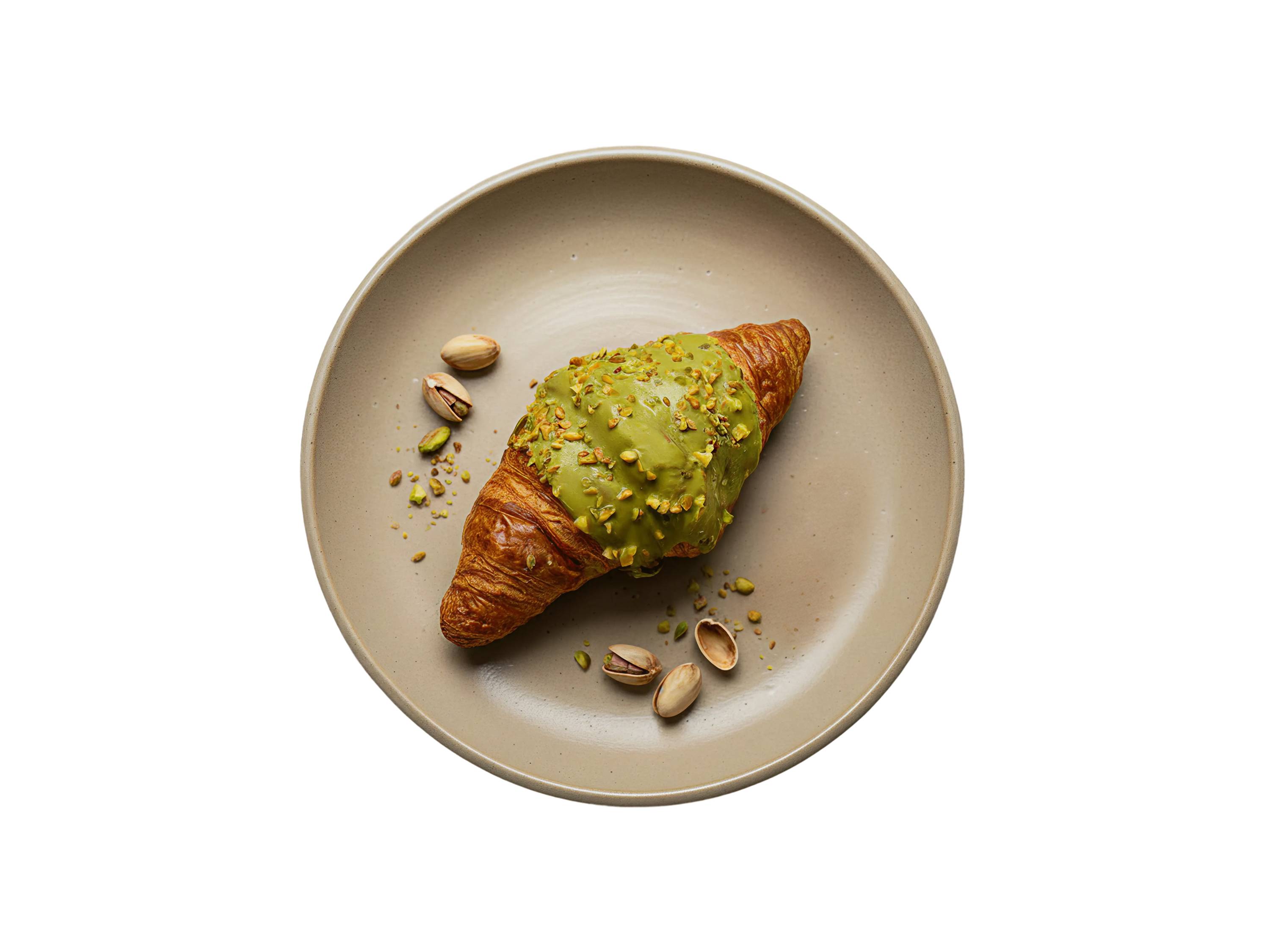 Croissant z polewą pistacjową i posypką z orzechów pistacjowych na talerzu.