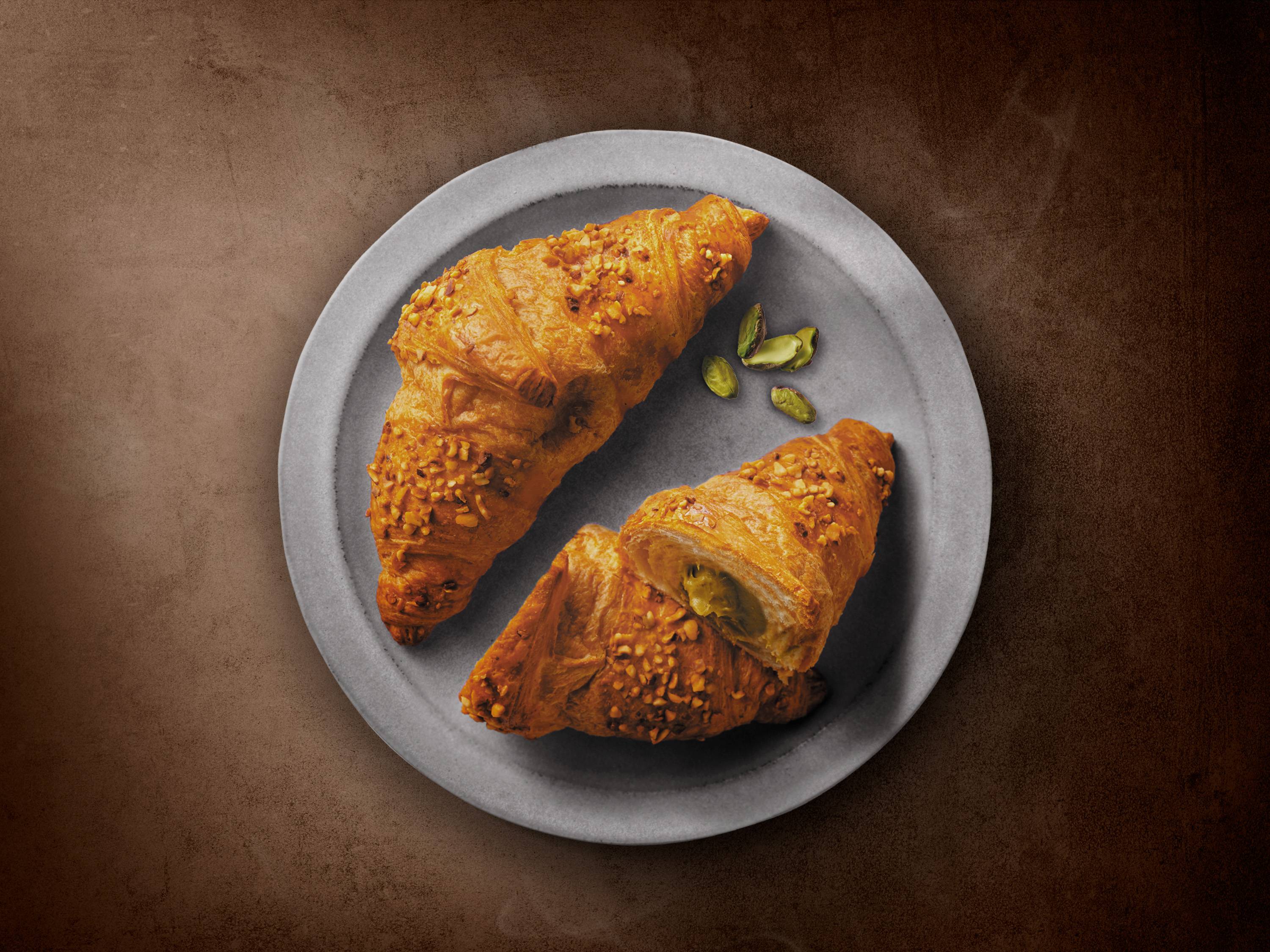 Dwa rogaliki z pistacjami i posypką orzechową na szarym talerzu.