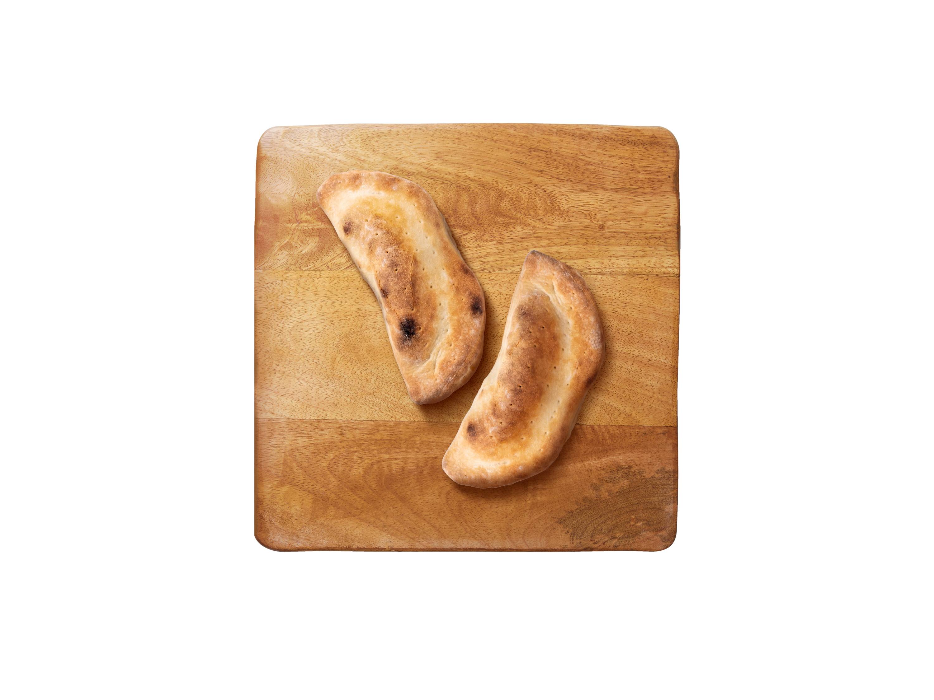 Dwa pieczone calzone na drewnianej desce do krojenia.