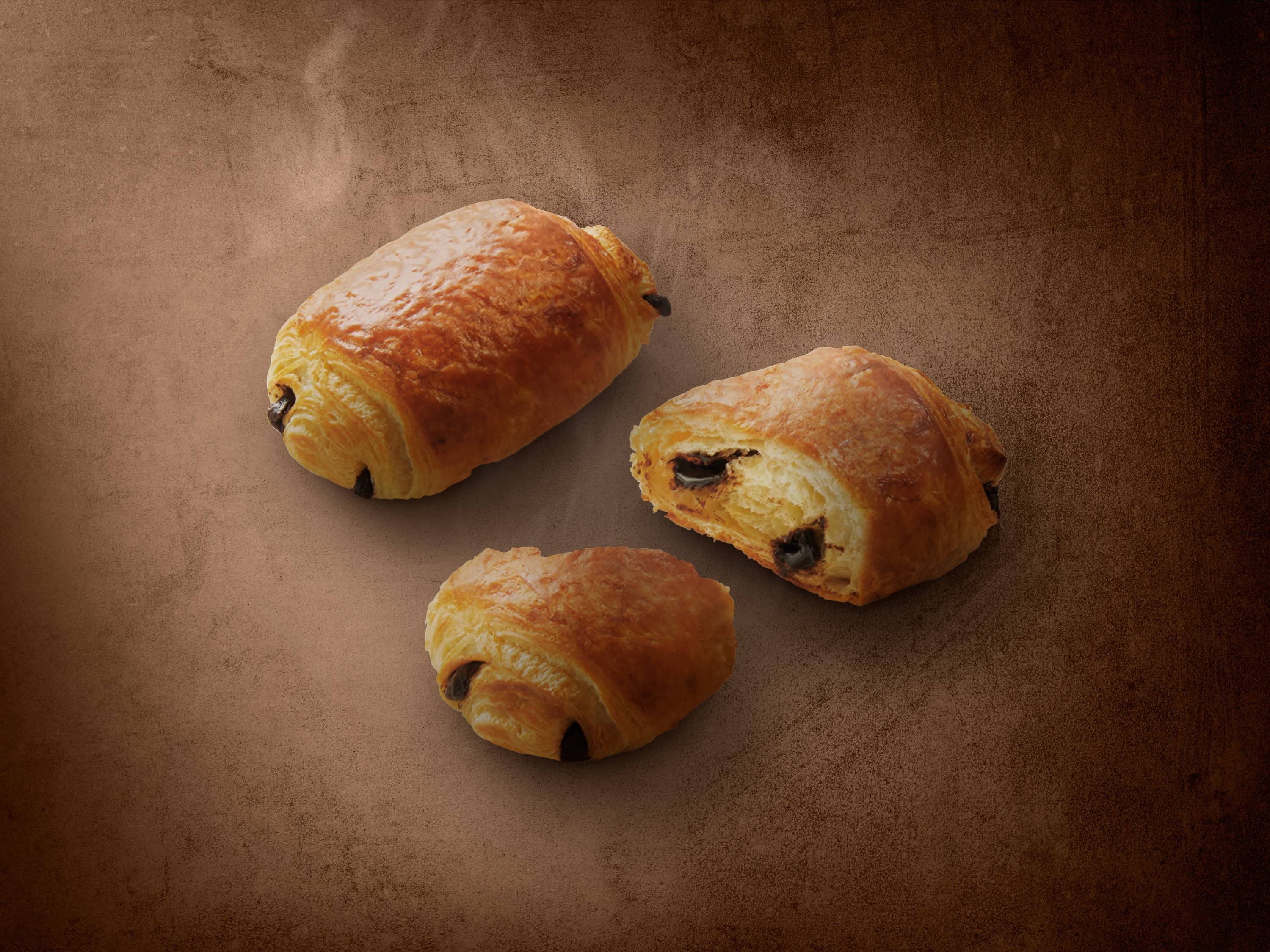 Trzy czekoladowe croissanty na brązowym tle.