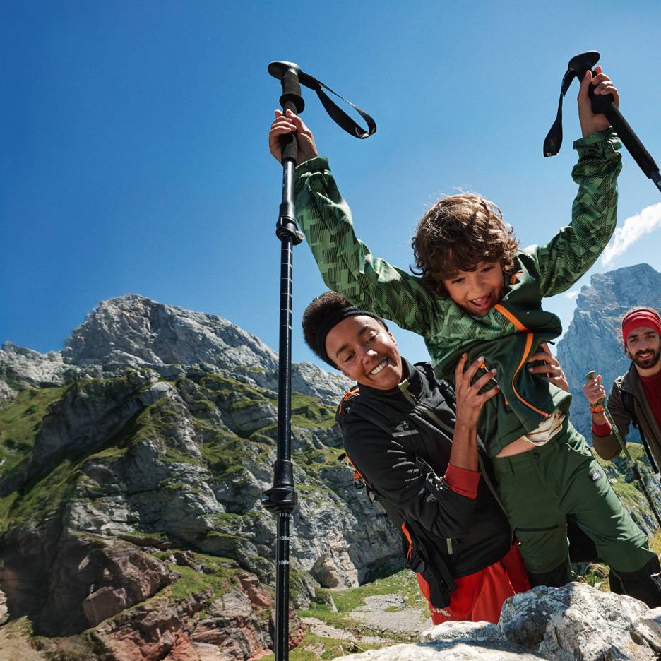 Rodzina wędrująca z kijkami trekkingowymi i odzieżą outdoorową w górach.
