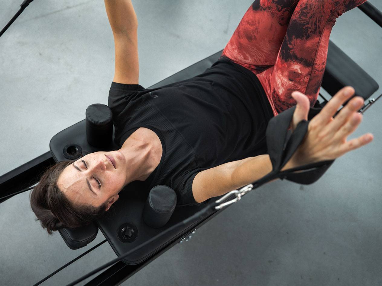 Kobieta w stroju sportowym leży na maszynie do Pilatesu, ćwicząc.