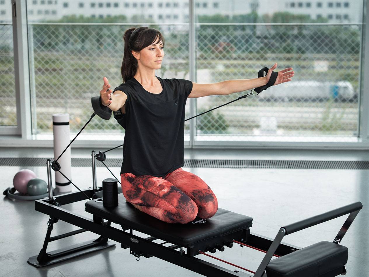 Kobieta ćwiczy Pilates na reformerze z taśmami oporowymi.