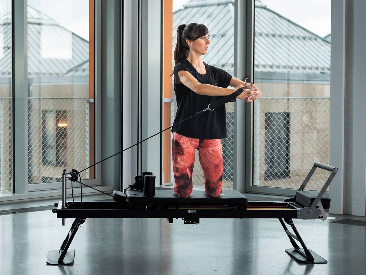 Kobieta ćwiczy Pilates na czarnej maszynie reformer w jasnym pokoju.