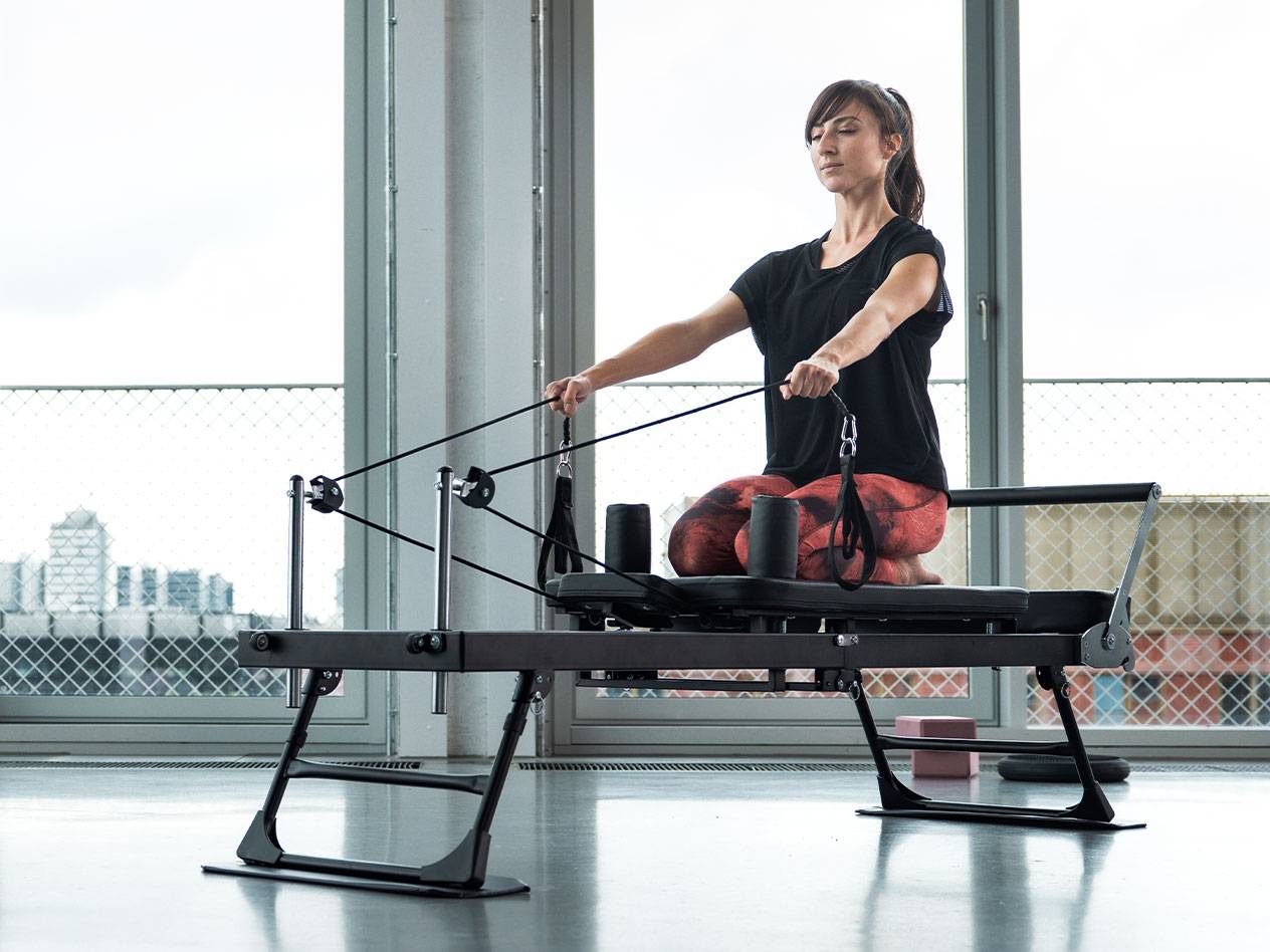 Kobieta ćwicząca Pilates na maszynie reformer z widokiem na miasto.