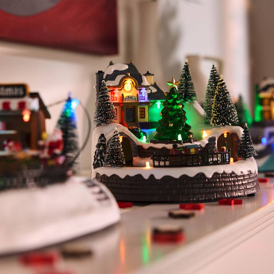 Wioska bożonarodzeniowa z oświetloną stacją, drzewami i miniaturową kolejką.