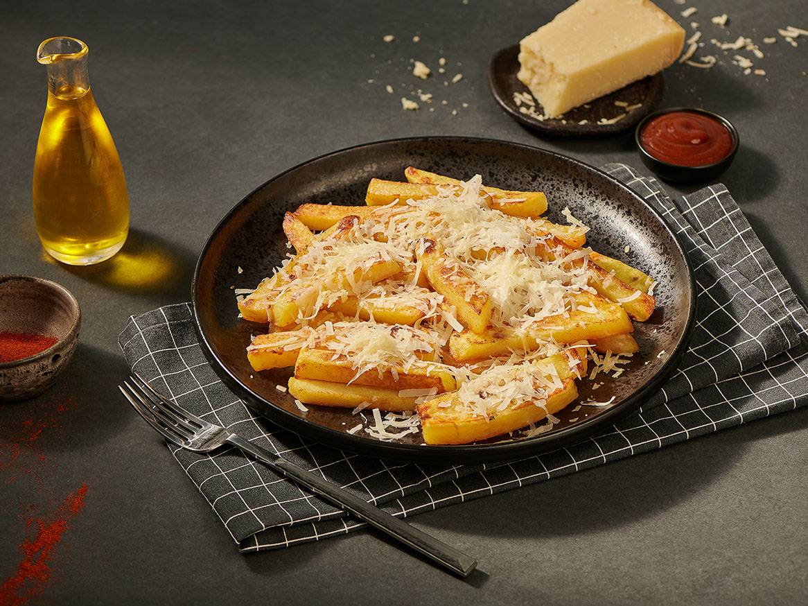 Frytki z parmezanem na czarnym talerzu, z oliwą, ketchupem i papryką.