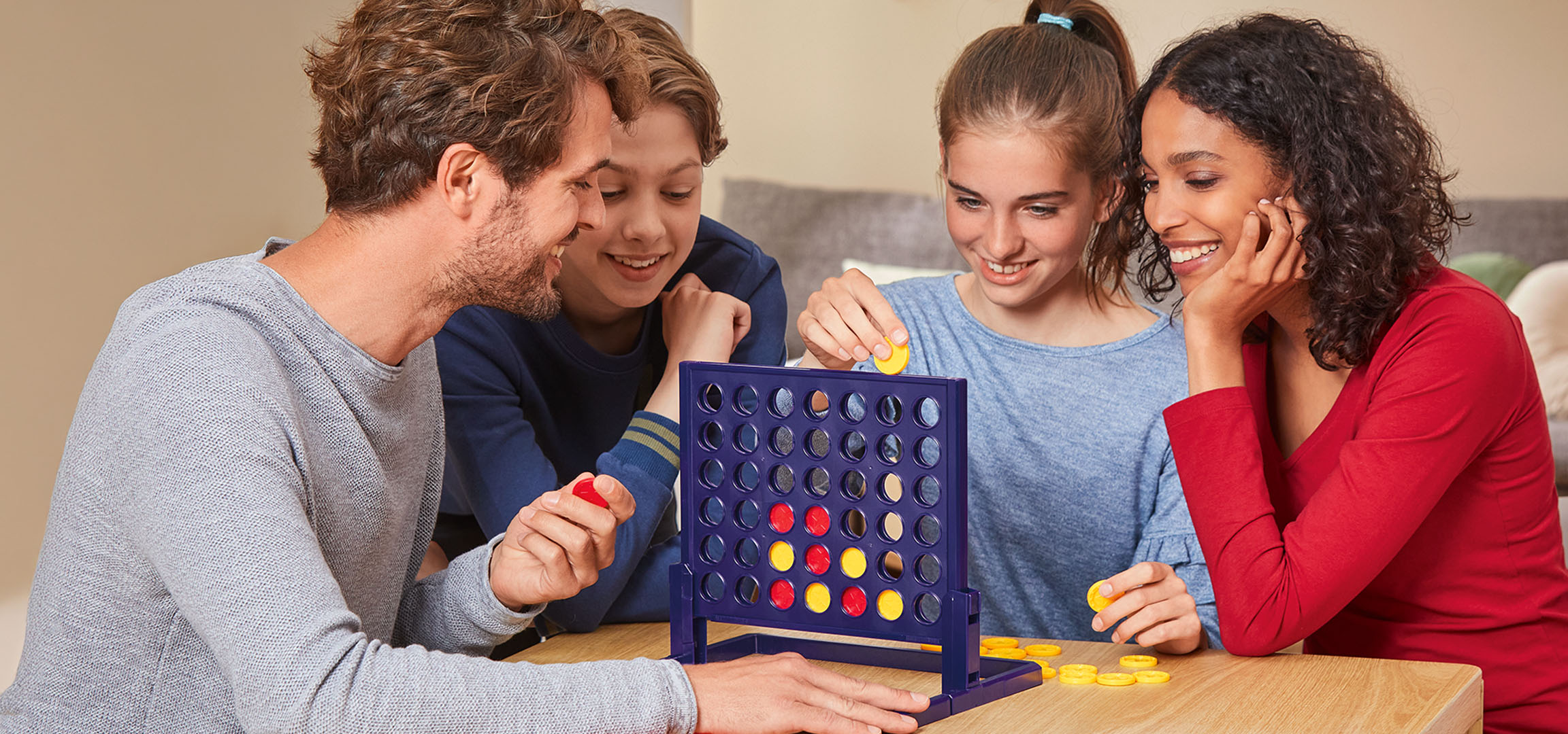 Cztery osoby grające w grę planszową Connect 4 przy drewnianym stole.