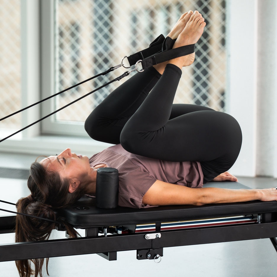 Kobieta ćwicząca Pilates na reformerze z nogami w paskach.