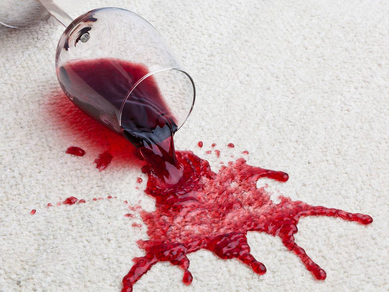 Czerwone wino rozlane ze szklanki na biały dywan