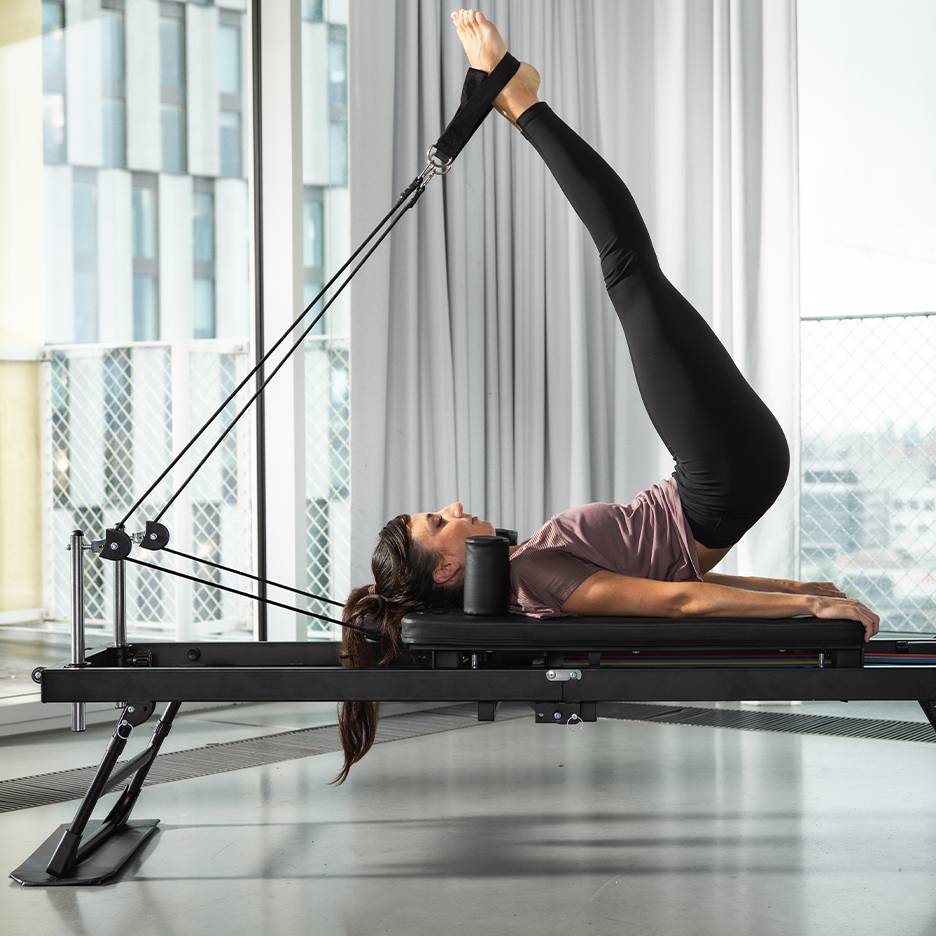 Kobieta ćwiczy Pilates na czarnej maszynie z nogami w górze.