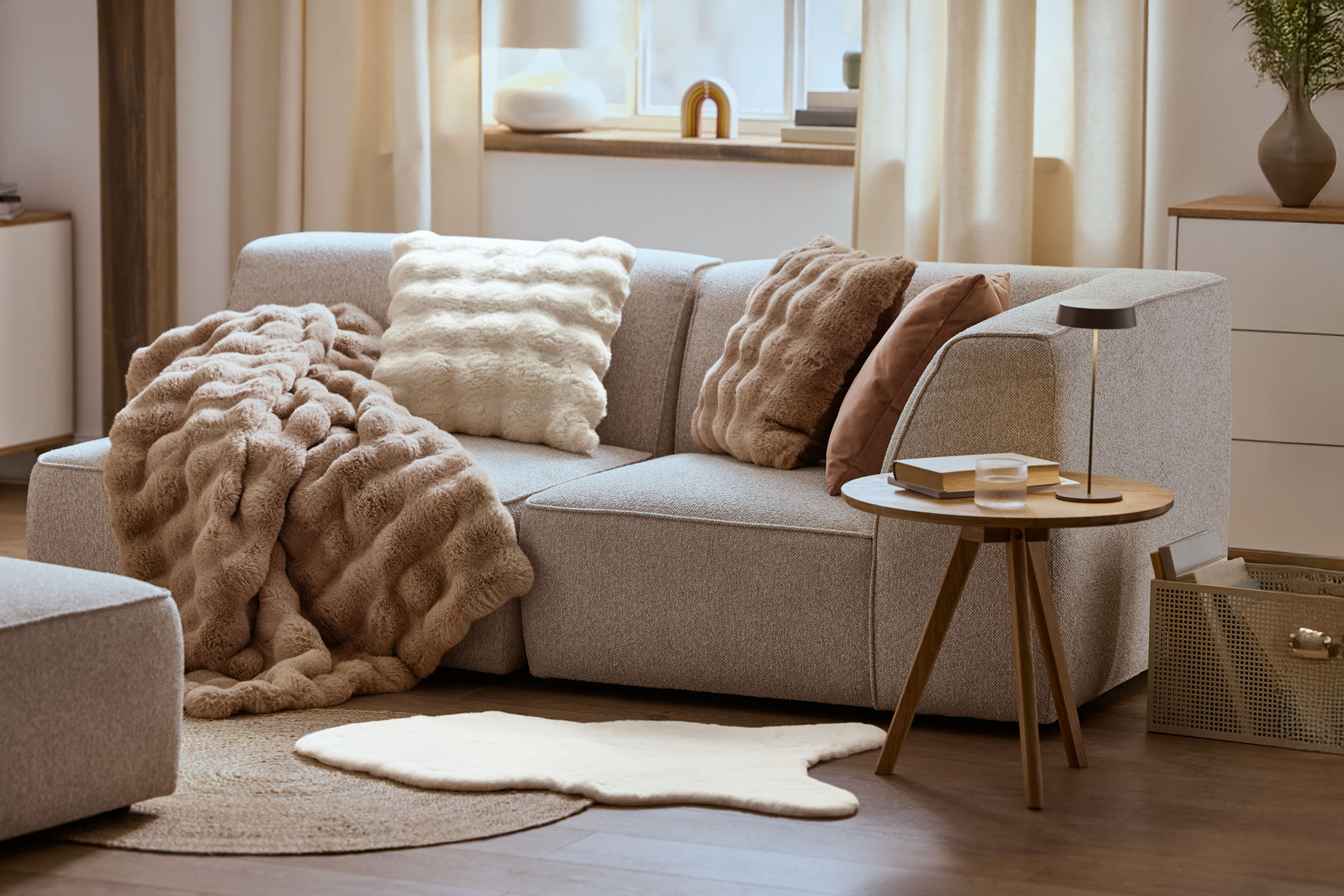 Przytulny salon z szarą sofą, puszystymi poduszkami i kocem, drewnianym stolikiem kawowym.