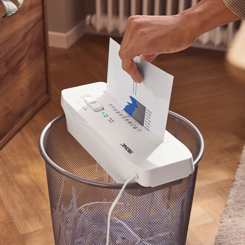 Ręka wkłada papier do niszczarki TRONIC umieszczonej na koszu na śmieci.