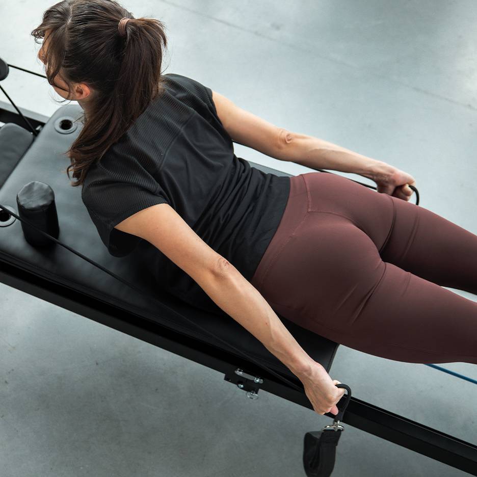 Kobieta ćwicząca na maszynie do pilatesu z taśmami oporowymi, w odzieży sportowej.