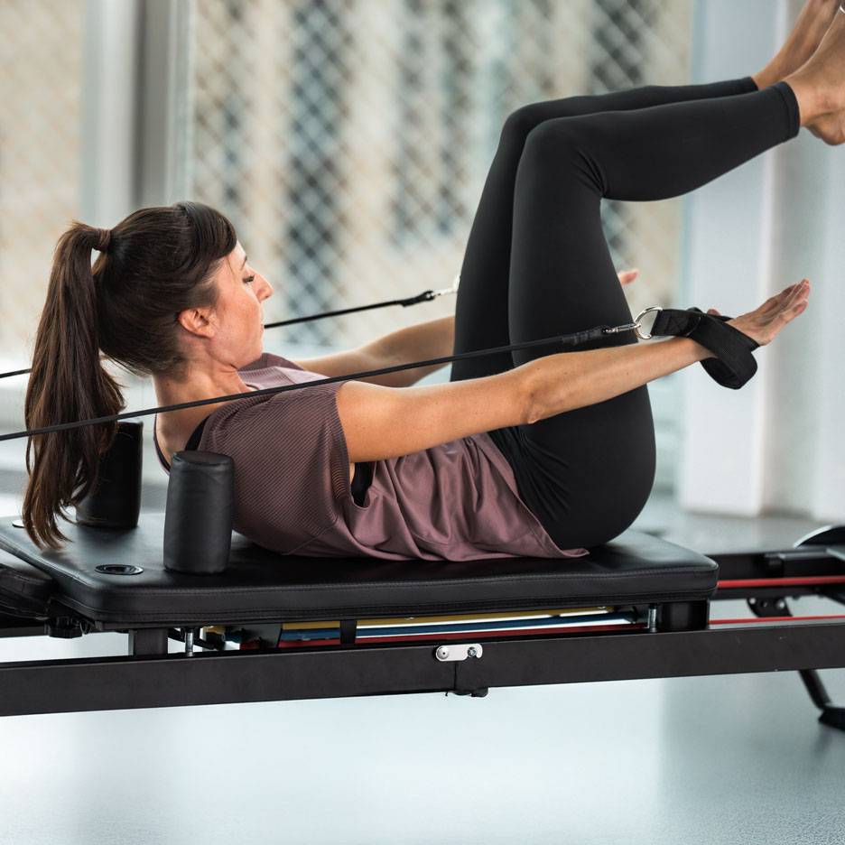 Kobieta ćwicząca Pilates na reformerze, ubrana w czarny strój sportowy.