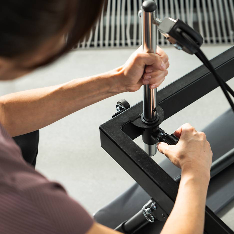 Osoba regulująca sprzęt fitness, skupiająca się na dłoniach i metalowych częściach.