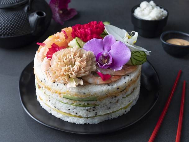 Tort sushi ozdobiony kwiatami, łososiem i krewetkami.