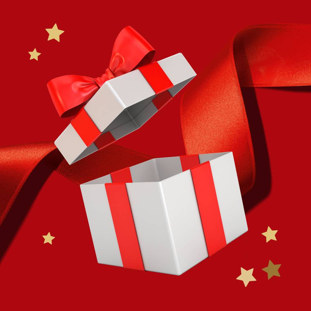 Otwarte białe pudełko prezentowe z czerwoną wstążką i złotymi gwiazdkami na czerwonym tle.