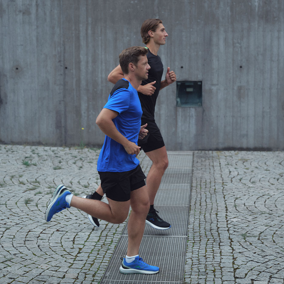 Dwóch mężczyzn w odzieży sportowej biegnie na zewnątrz po brukowanej ulicy.