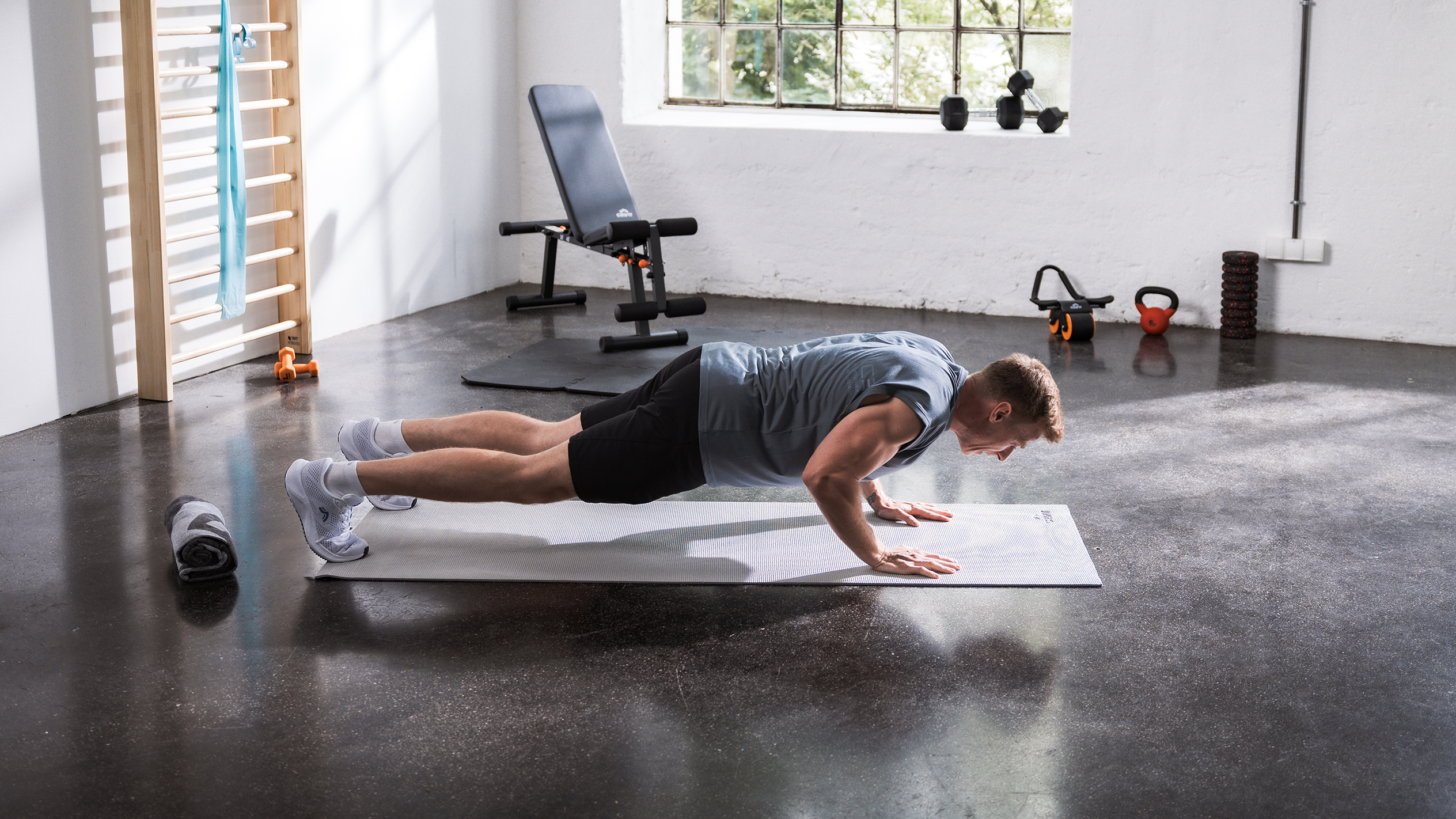 Mężczyzna robi pompki na macie w domowej siłowni z różnym sprzętem fitness.