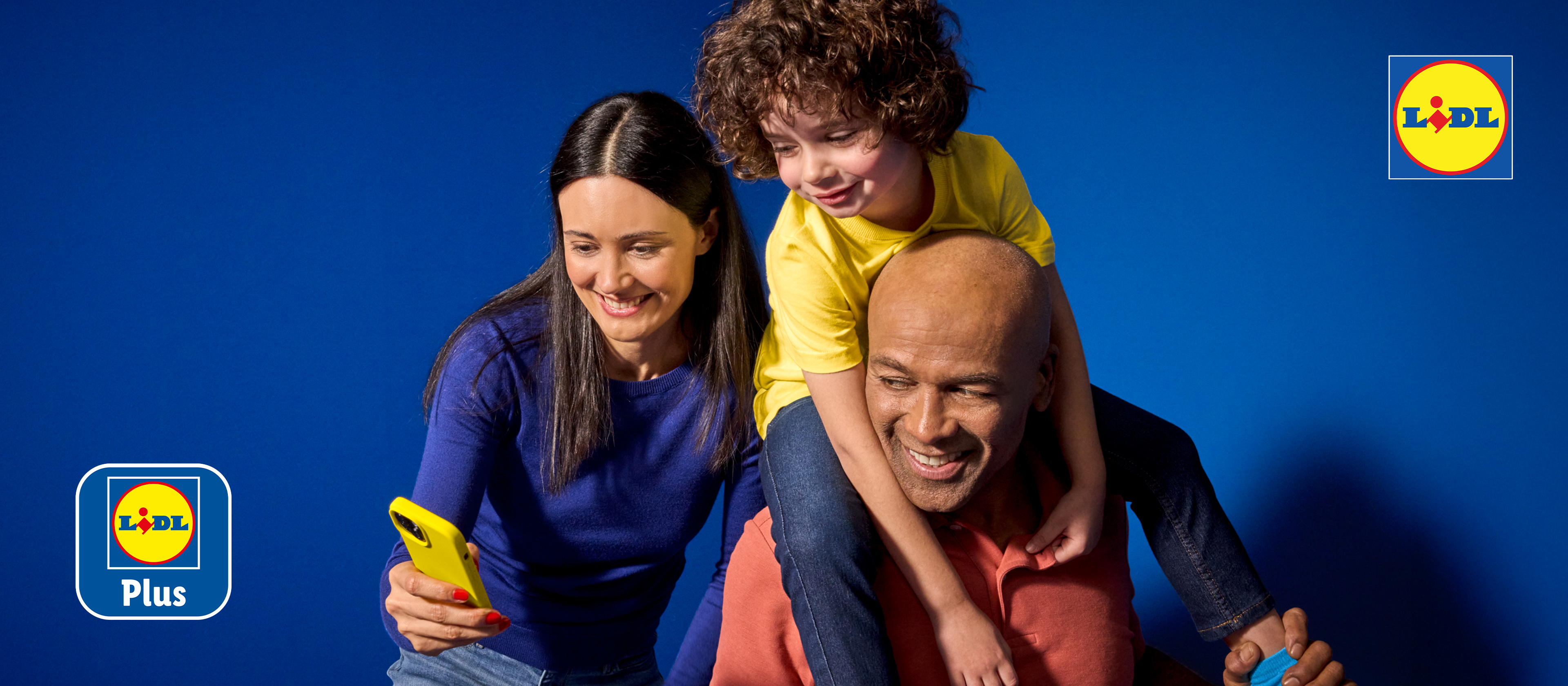 Rodzina z dzieckiem na barana, kobieta trzyma smartfon, logo programu lojalnościowego.