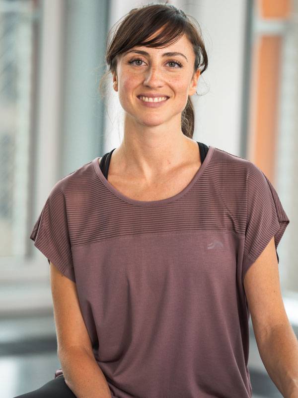 Uśmiechnięta kobieta w fioletowym sportowym topie z krótkim rękawem.