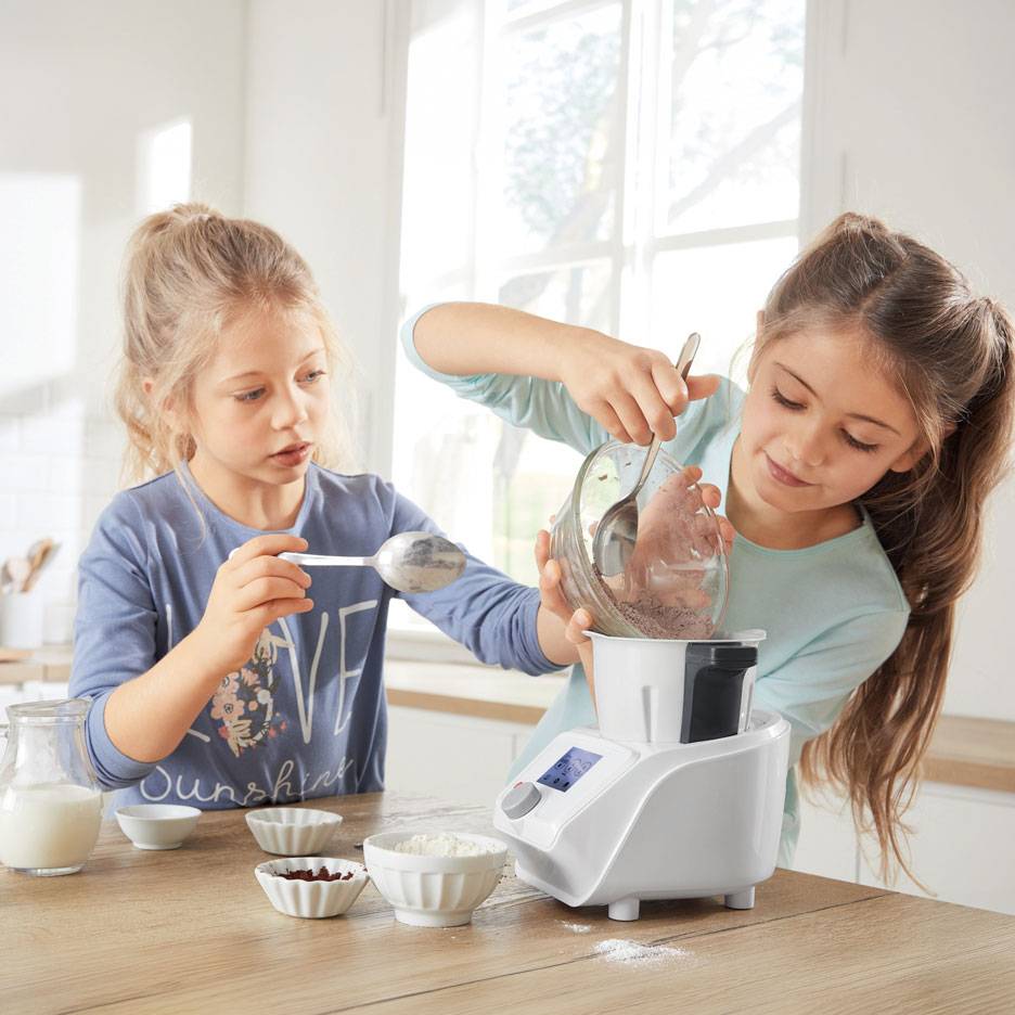 Dwie dziewczynki przygotowują ciasto w robocie kuchennym, na stole stoją miseczki ze składnikami.