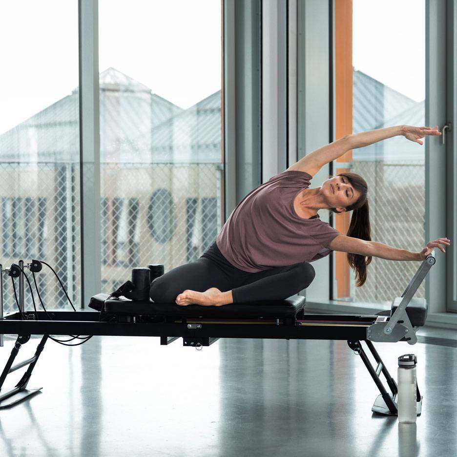 Kobieta ćwiczy pilates na reformerze, rozciągając się na boki.