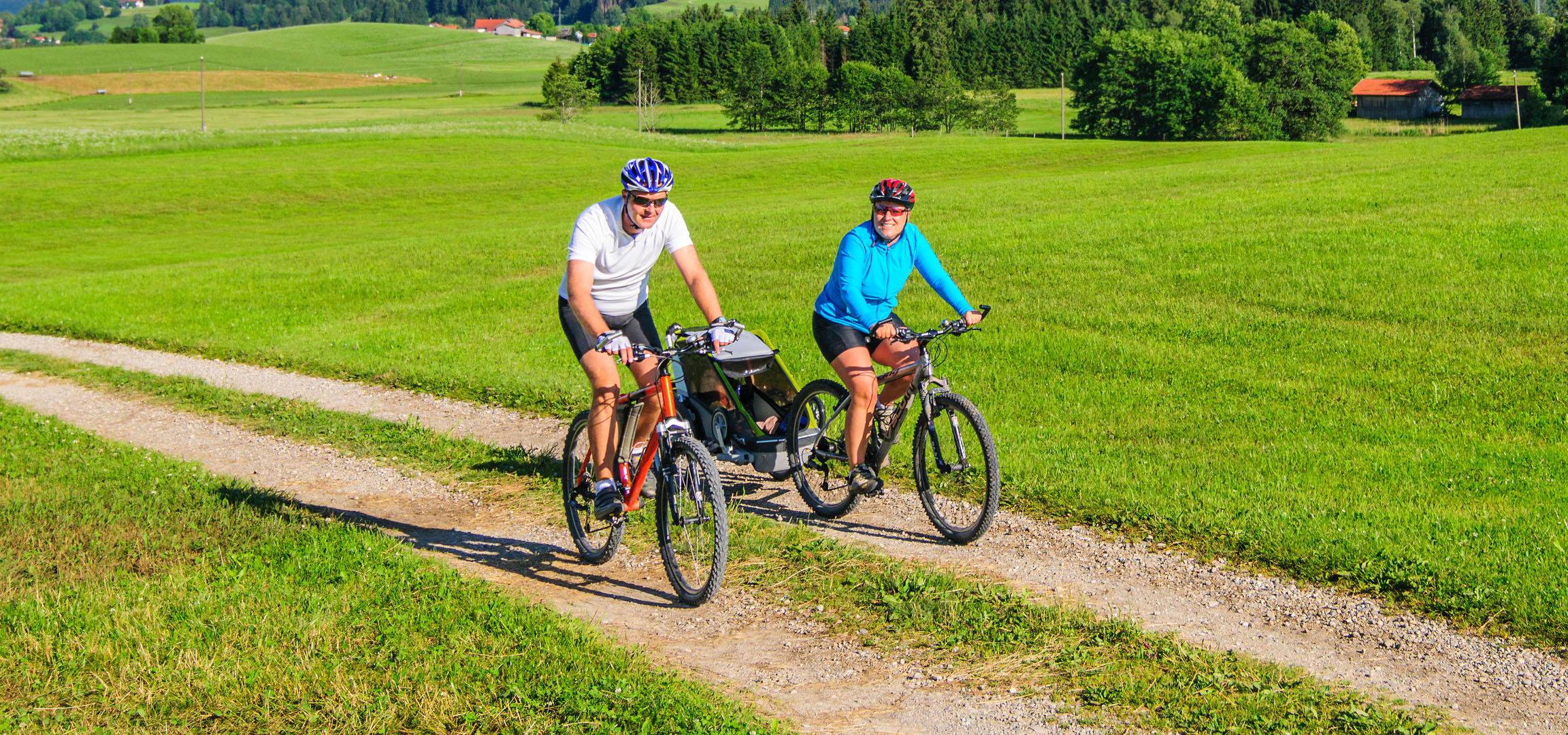 Para jeździ na rowerach w zielonym krajobrazie.