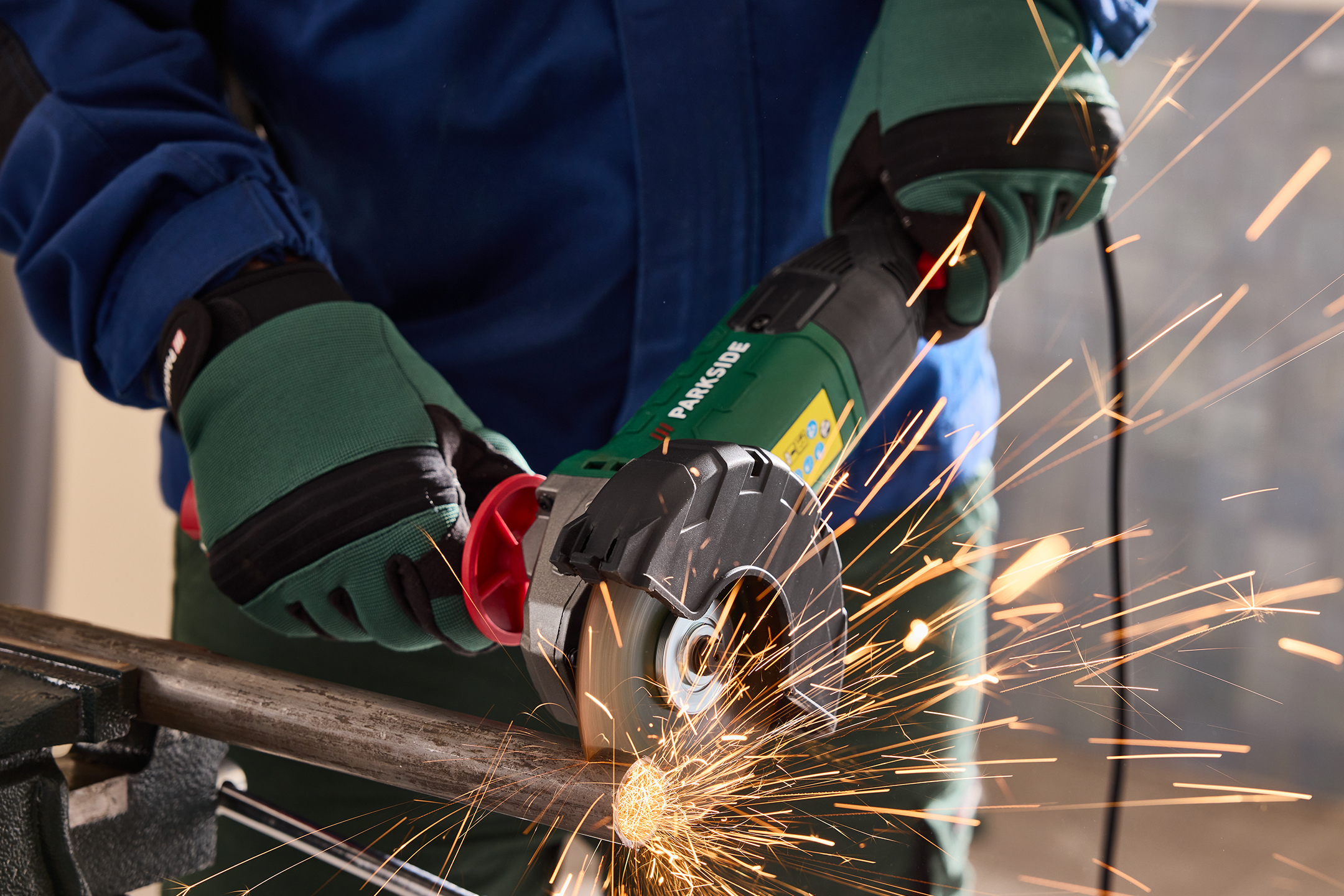 Osoba w rękawicach ochronnych używająca szlifierki kątowej do cięcia metalowej rury, z iskrami.