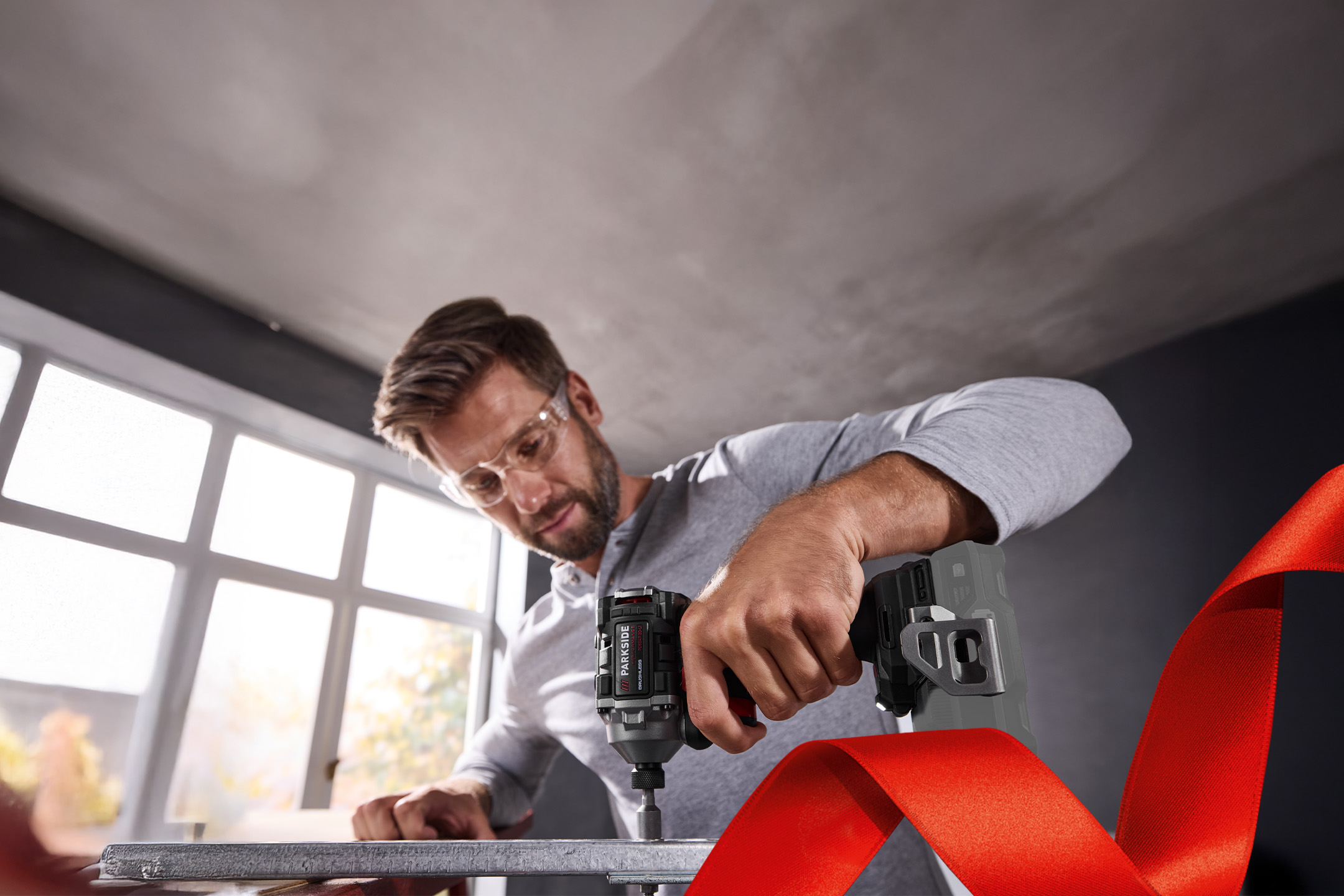 Mężczyzna w okularach ochronnych używający wkrętarki udarowej Parkside do montażu metalowej konstrukcji.