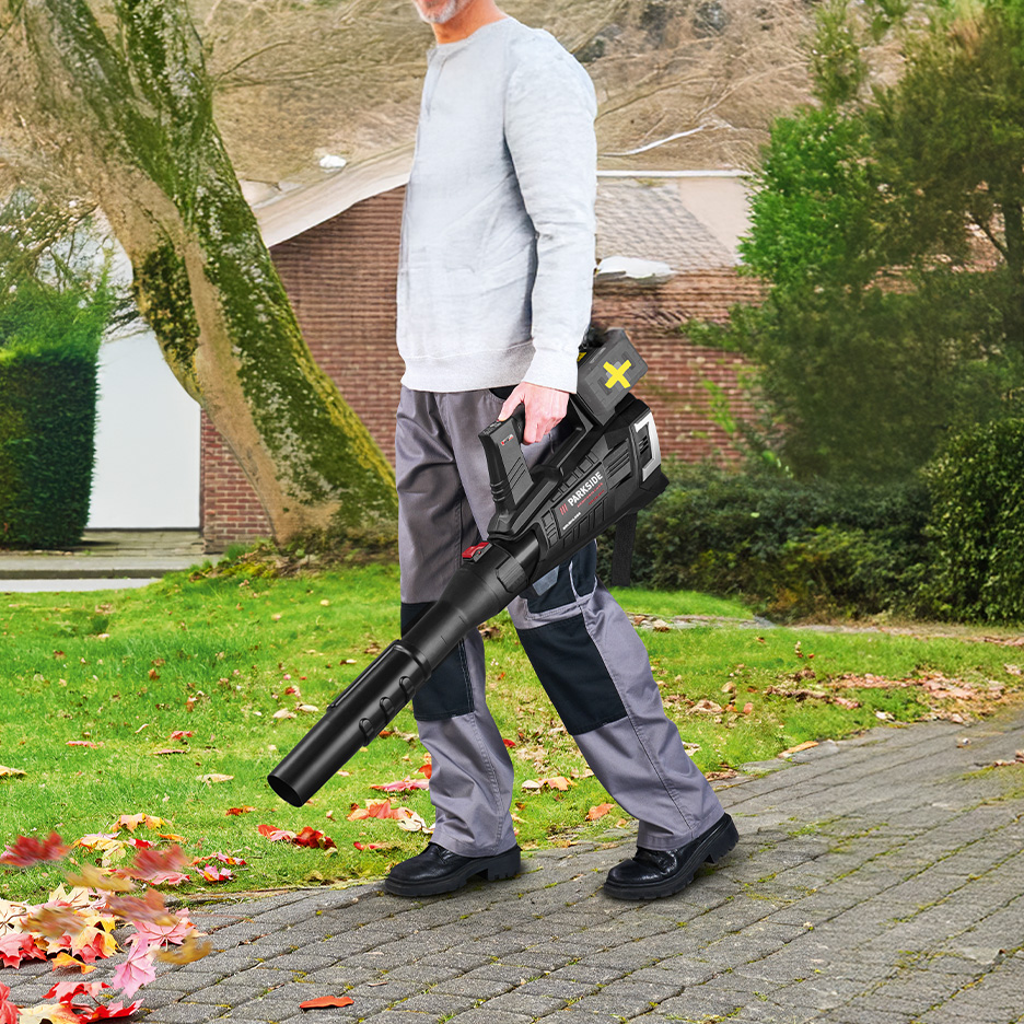 Mężczyzna używa dmuchawy do liści Parkside z akumulatorem, sprzątając liście z chodnika.