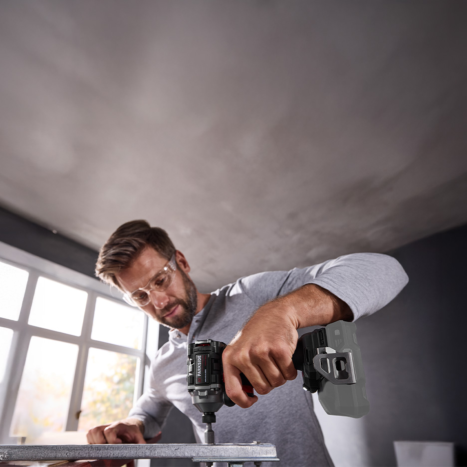 Mężczyzna w okularach ochronnych używa wiertarko-wkrętarki Parkside do pracy z metalem.